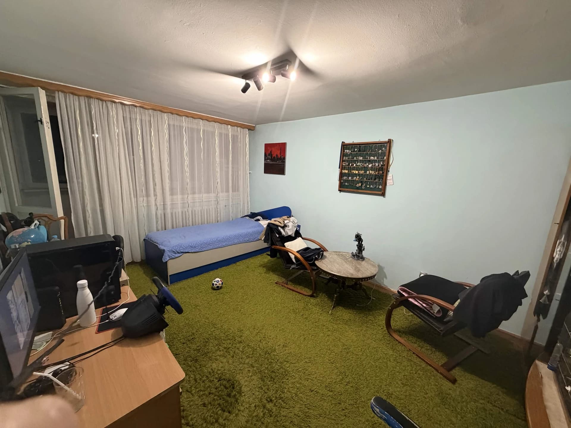 The real RoomTest interior, with pale blue walls, green carpet, a blue daybed, desks, and two wooden armchairs around a round table.